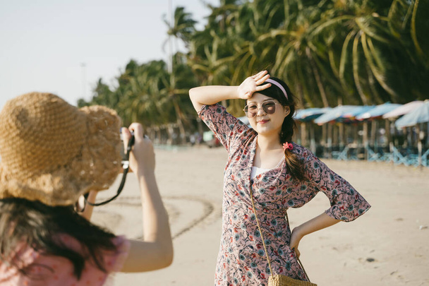 Tyttö yllään hattu ottaa kuvan hänen ystävänsä, kun he kävelevät rannalla tuulisena päivänä. - Valokuva, kuva