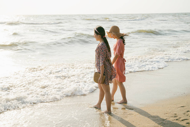 Két lány együtt sétál a parton, nézik a hullámokat a tengerből.. - Fotó, kép
