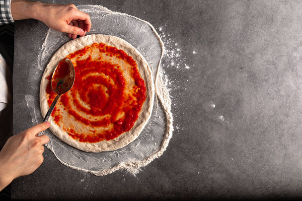 Φτιάχνοντας μια πίτσα απλώνοντας σάλτσα ντομάτας στη ζύμη - Φωτογραφία, εικόνα