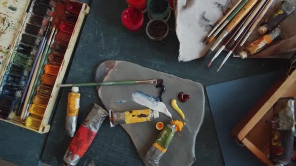Top down tracking shot of watercolor paint set, palette, brushes and paint tubes in wooden case on table in art studio - Footage, Video