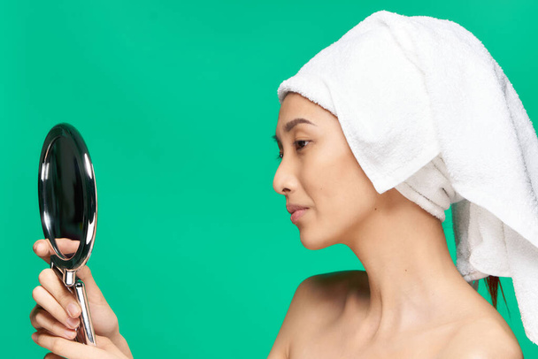 όμορφη χαμογελαστή γυναίκα με έναν καθρέφτη στα χέρια της μια πετσέτα στο κεφάλι της φροντίδα του δέρματος πράσινο φόντο - Φωτογραφία, εικόνα