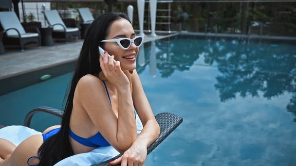 glückliche Frau mit Sonnenbrille, die auf der Sonnenbank liegt und mit dem Smartphone spricht - Foto, Bild