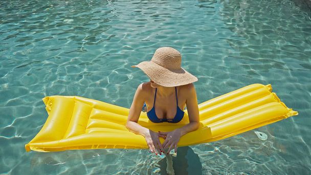 Frau mit Strohhut schwimmt im Pool mit gelber aufblasbarer Matratze - Foto, Bild