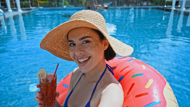 χαρούμενη γυναίκα κρατώντας κοκτέιλ και κολύμπι στην πισίνα με δαχτυλίδι κολύμβησης  - Φωτογραφία, εικόνα