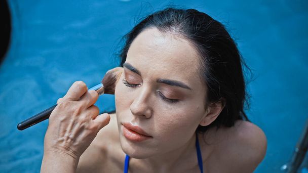 sminkes alkalmazó arc por kozmetikai kefe fiatal nő medence közelében  - Fotó, kép