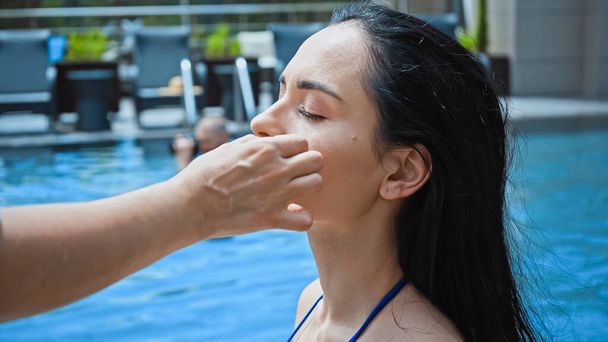 Makyaj sanatçısı havuz kenarındaki esmer kadına yüz temeli uyguluyor.  - Fotoğraf, Görsel