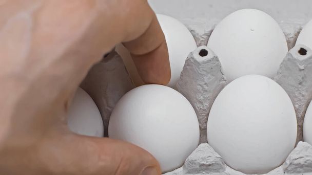 abgeschnittene Ansicht eines Mannes, der ein Ei aus der Verpackung nimmt, Nahaufnahme - Foto, Bild