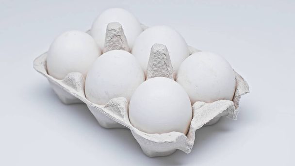 шесть куриных яиц в картонной упаковке на белой поверхности - Фото, изображение