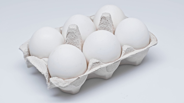Beyaz yüzeyde karton pakette altı tavuk yumurtası. - Fotoğraf, Görsel