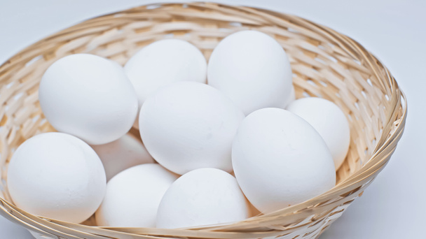 άφθονα αυγά κοτόπουλου σε ψάθινο καλάθι σε λευκή επιφάνεια - Φωτογραφία, εικόνα