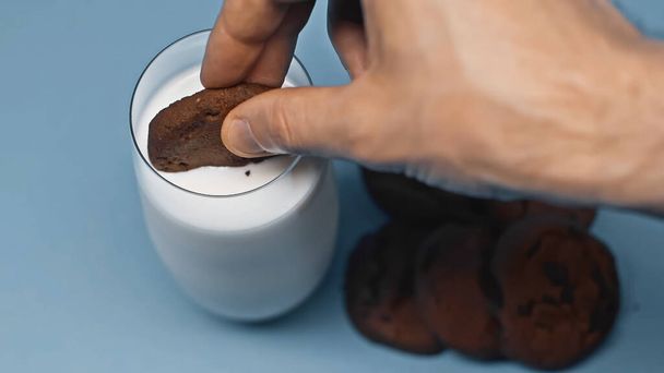 partial view of man dipping chocolate cookie in fresh milk on blue - Photo, Image