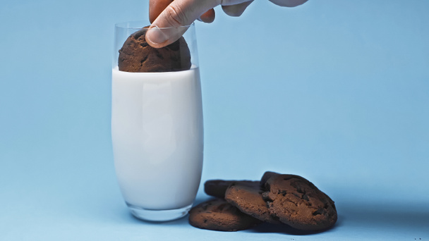 vista parcial del hombre sumergiendo deliciosa galleta de chocolate en leche fresca en azul - Foto, Imagen