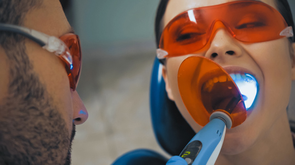 οδοντίατρος που χρησιμοποιεί υπεριώδη λάμπα σε ασθενή σε γυαλιά, θολή πρώτο πλάνο - Φωτογραφία, εικόνα