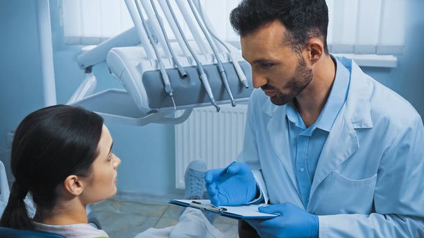 hammaslääkäri tilalla leikepöydälle puhuessaan potilaalle lähellä hampaiden välineitä - Valokuva, kuva