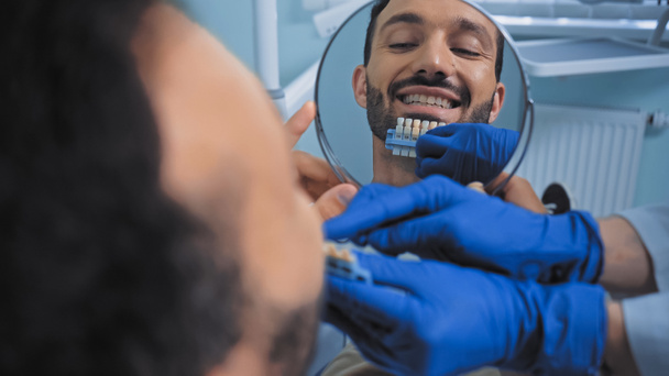 stomatologist holding teeth color palette near smiling patient, blurred foreground - Photo, Image