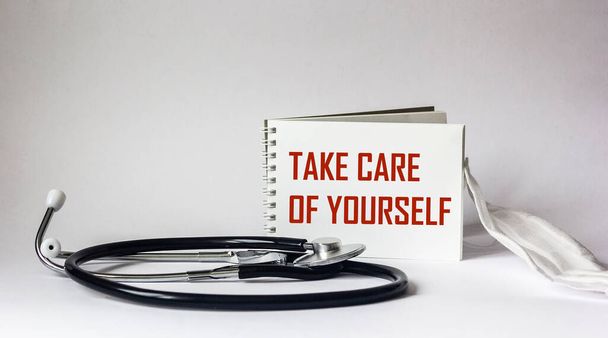 Κείμενο φροντίζει τον εαυτό σας σε ένα notebook, κοντά σε ένα stethoscope και ένα ιατρικό χάρτη σε ένα λευκό φόντο - Φωτογραφία, εικόνα