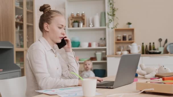 Steadicam της νεαρής κατειλημμένης Καυκάσιας μητέρας κάθεται στο γραφείο, έχοντας σημαντική επαγγελματική κλήση στο smartphone, πληκτρολογώντας σε φορητό υπολογιστή, στη συνέχεια κλείνοντας και πιάνοντας παιχνιδιάρικο νήπιο - Πλάνα, βίντεο