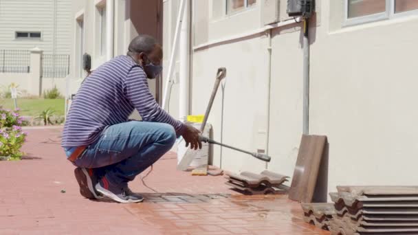 Cleaning tile with water pressure washer. Janitor sprays city street sidewalk paving slabs. Black man disinfects floor and surfaces from coronavirus. Antibacterial sanitary measures on quarantine. - Footage, Video