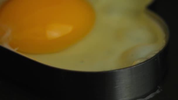 Cocinar el huevo frito en forma de corazón en una sartén. Cocinar un desayuno sorpresa para el 8 de marzo. Vista macro - Metraje, vídeo