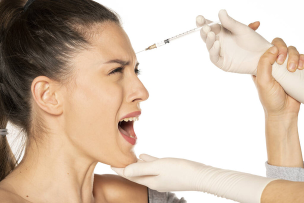 Portret van een jonge bange vrouw op een gezichtsvuller injectieprocedure op witte achtergrond - Foto, afbeelding