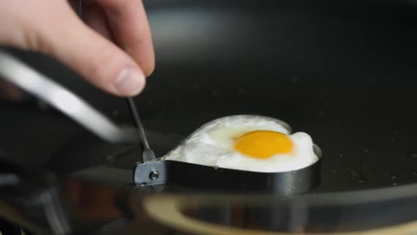 Gefrituurd ei koken in de vorm van een hart in een koekenpan. Het ei op een bord leggen. Een verrassingsontbijt klaarmaken voor 8 maart - Video
