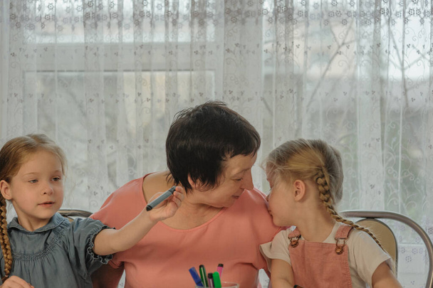granddaughter kissing grandmother at home while drawing - Photo, Image