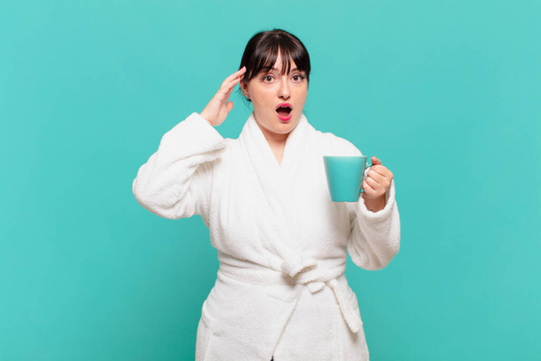 young woman wearing bathrobe looking happy, astonished and surprised, smiling and realizing amazing and incredible good news - Фото, изображение