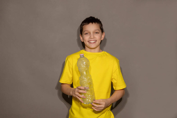 Boy teenager volunteer holding plastic bottle on gray background in studio and smiling. Zero plastic, Recycling concept. Copy space - Valokuva, kuva