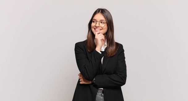 young business woman smiling with a happy, confident expression with hand on chin, wondering and looking to the side - Foto, Imagen