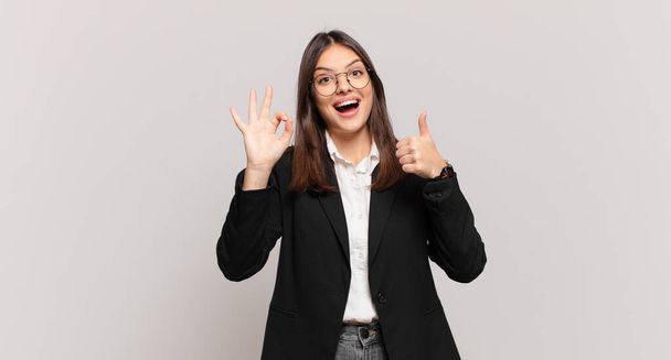 young business woman feeling happy, amazed, satisfied and surprised, showing okay and thumbs up gestures, smiling - Φωτογραφία, εικόνα