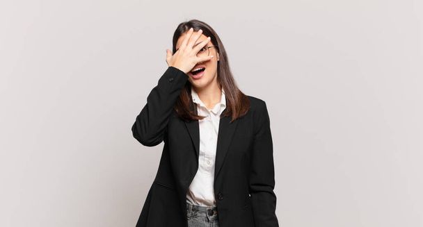 young business woman looking shocked, scared or terrified, covering face with hand and peeking between fingers - Photo, image