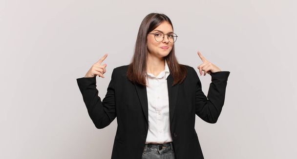 young business woman with a bad attitude looking proud and aggressive, pointing upwards or making fun sign with hands - Фото, изображение