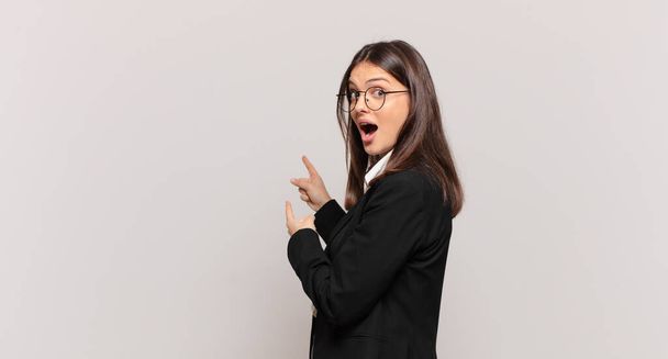 young business woman feeling shocked and surprised, pointing to copy space on the side with amazed, open-mouthed look - Foto, immagini