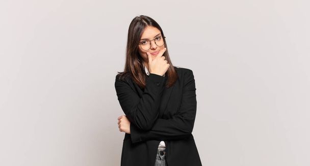 young business woman looking serious, thoughtful and distrustful, with one arm crossed and hand on chin, weighting options - Photo, image