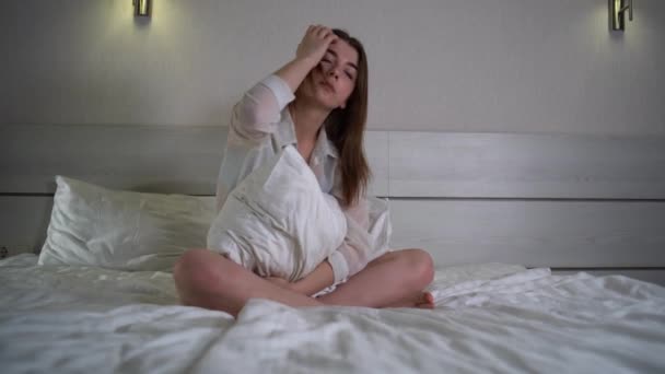 Грустная задумчивая одинокая кавказская женщина с задумчивым лицом, обнимающая подушку, сидящая на кровати, думающая о проблемах, сидящая одна дома, расстроенная женщина, чувствующая депрессию,  - Кадры, видео