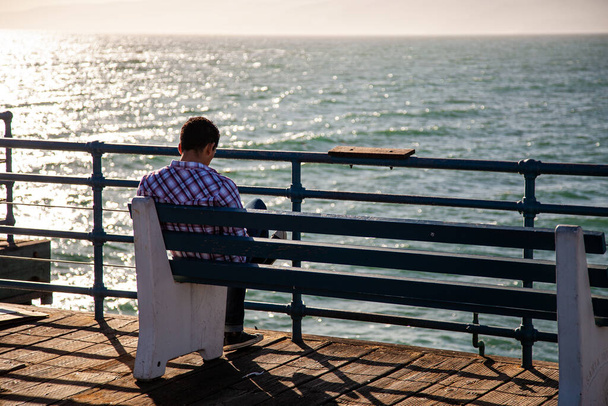 Man sitting reading on a pier overlooking the ocean - Photo, Image
