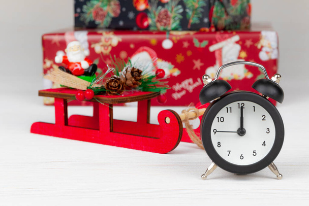 Święty Mikołaj na saniach, pudełka z prezentami i budzik na białym tle drewna - Zdjęcie, obraz