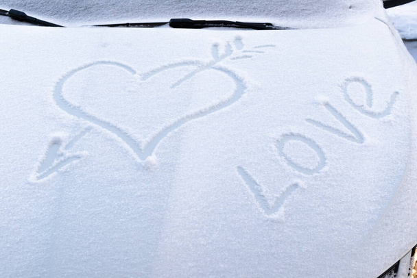 Bild eines gebrochenen Herzens mit einem Pfeil im Schnee auf der Motorhaube eines Autos an einem frostigen Wintertag - Foto, Bild