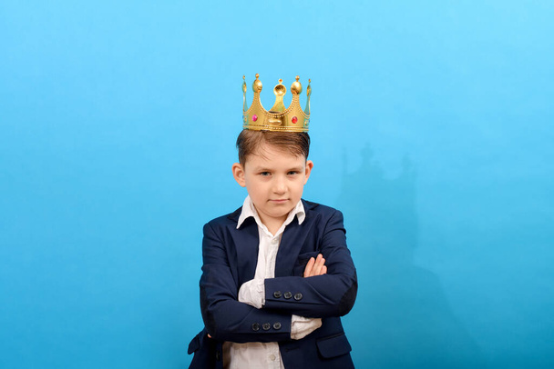 Junge im Anzug und mit goldener Krone auf dem Kopf auf blauem Grund. Herrschaft und Macht über andere. - Foto, Bild