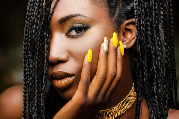 Elleri yanağında büyüleyici bir Afrikalı kadının güzel portresi. Örülmüş saç stili ve esmer arka planda şehvetli görünüşlü bir kız..  - Fotoğraf, Görsel