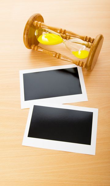 空白のインスタント写真や木製のテーブルの上の時間ガラス - 写真・画像