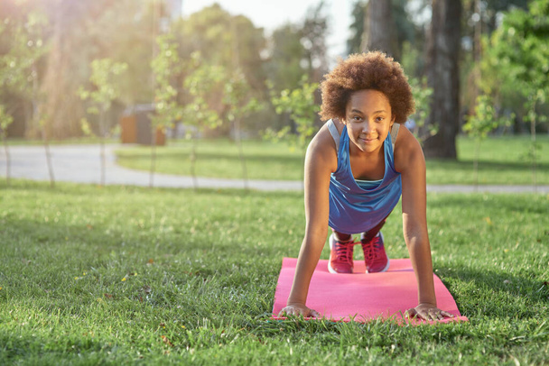 Radosna dziewczynka robi deskę na macie do jogi w parku - Zdjęcie, obraz