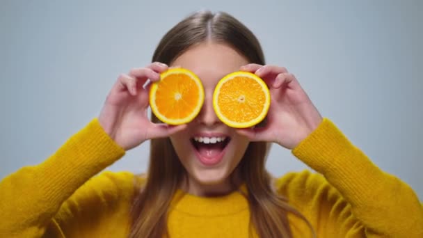 Portret wesołej kobiety bawiącej się dwoma plastrami pomarańczy w studio. - Materiał filmowy, wideo