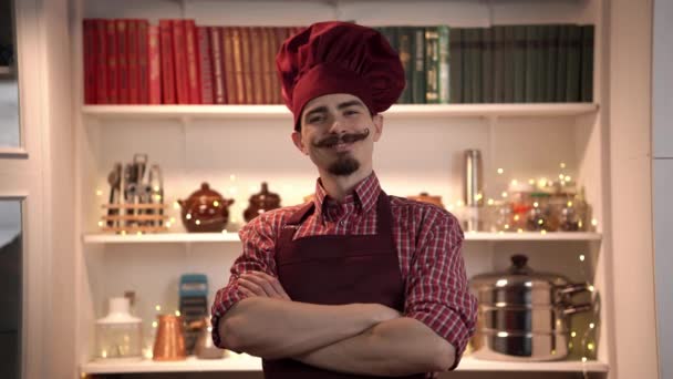 Πορτρέτο του χαμογελαστού νέου μάγειρα φορώντας κόκκινη τουαλέτα με ποδιά και στέκεται με σταυρωμένα χέρια - Πλάνα, βίντεο