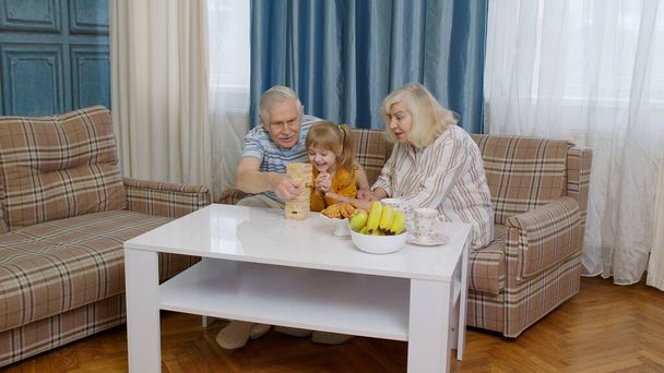 Garota criança animado envolvido na construção blocos jogo de tabuleiro com avó sênior e avô - Foto, Imagem