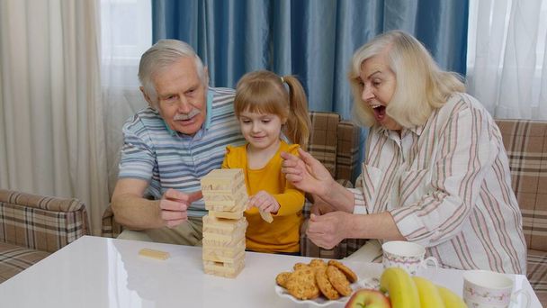 Ηλικιωμένοι παππούδες ζευγάρι και εγγονή απολαμβάνοντας επιτραπέζιο παιχνίδι κτίριο πύργο από μπλοκ στο σπίτι - Φωτογραφία, εικόνα
