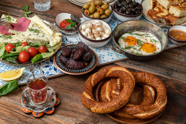 Delicioso y rico desayuno turco tradicional incluye tomates, pepinos, queso, mantequilla, huevos, miel, pan, rosquillas, aceitunas y tazas de té. Ramadan Suhoor aka Sahur (comida de la mañana antes del ayuno).  - Foto, Imagen
