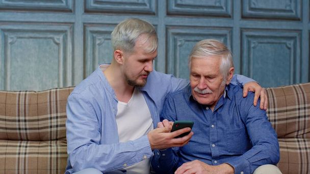 Happy famille père aîné et fils regardant sur téléphone mobile à Internet en ligne avec plaisir ensemble - Photo, image