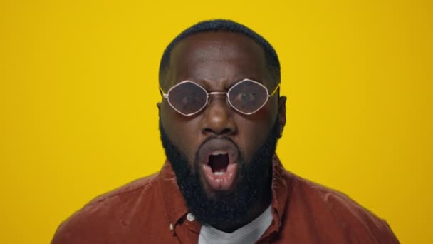 Portrait of angry african man screaming in sunglasses on yellow background. - Footage, Video