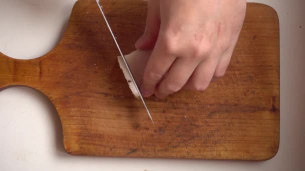 Рука режет большой кусок соленого жира на мелкие кусочки ножом на деревянной доске - Кадры, видео